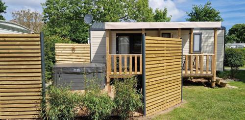a wooden cabin with a porch in the grass at Mobil-home Premium avec spa privatif in Pordic