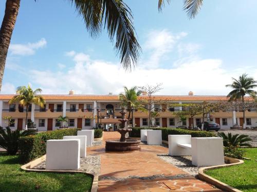 - un bâtiment avec une cour dotée de chaises blanches et de palmiers dans l'établissement Hotel Torre Molino, à Monte Gordo