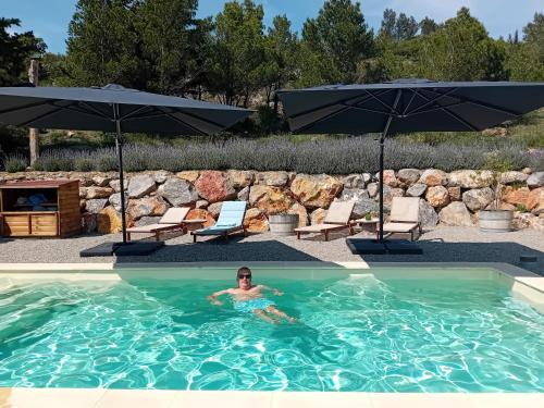 un homme dans une piscine à côté de deux parasols dans l'établissement MaCoCo Maison Coeur Corbieres, à Fontjoncouse