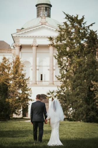 a bride and groom walking in front of a building at Hotel Zámok Topoľčianky in Topoľčianky
