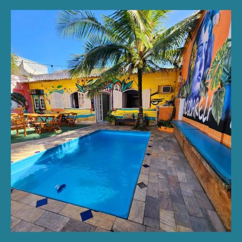a swimming pool in front of a house with a palm tree at Acquarela Hostel in Arraial do Cabo