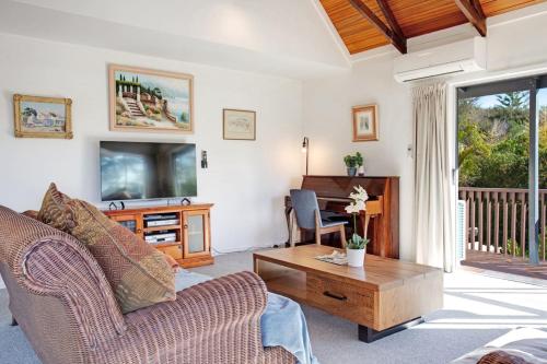 a living room with a couch and a tv and a table at Torbay Sun Drenched Villa near Local Beaches in Auckland