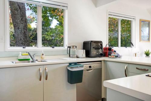 a kitchen with white counters and two windows at Torbay Sun Drenched Villa near Local Beaches in Auckland