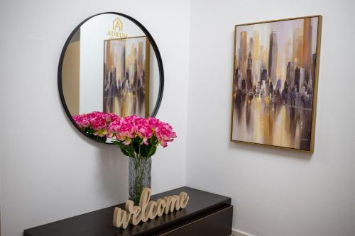 a vase of pink flowers on a table with a mirror at Aurum apartman Žepče in Žepče