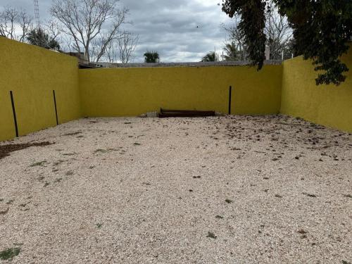 a yellow wall with a dirt ground next to a fence at Hotel Poquito a Poquito in Valladolid