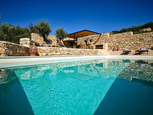 a swimming pool with blue water and a stone wall at Pezoules House in Lefkes