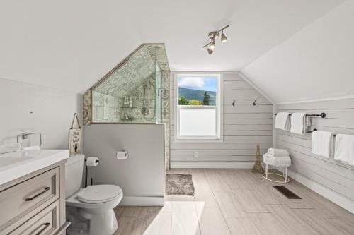 a white bathroom with a toilet and a window at Stunning Heritage Home, Sleep 10, Hot Tub, Private Yard, Firepit, in Vernon