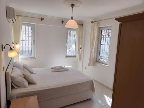 a white bedroom with a bed and two windows at Villa Yelken Oludeniz in Ovacik