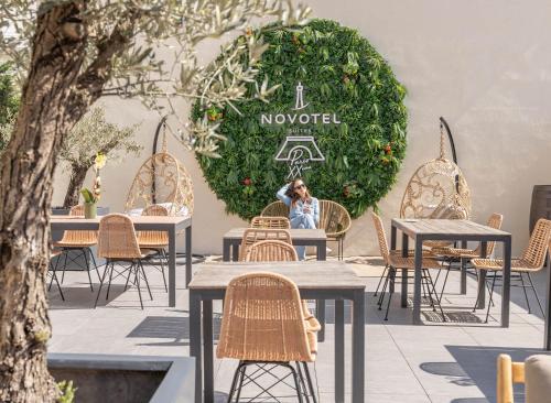 a woman sitting at a table in front of a green hedge at Novotel Suites Paris Montreuil Vincennes in Paris