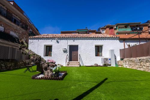 ein weißes Haus mit einem grünen Garten mit einem Baum in der Unterkunft Casa Postiguillo in Manzanares el Real