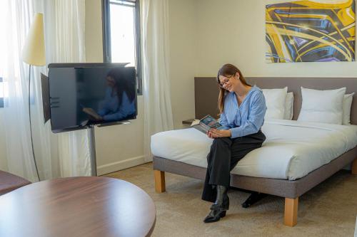 a woman sitting on a bed reading a book at Novotel Suites Paris Montreuil Vincennes in Paris