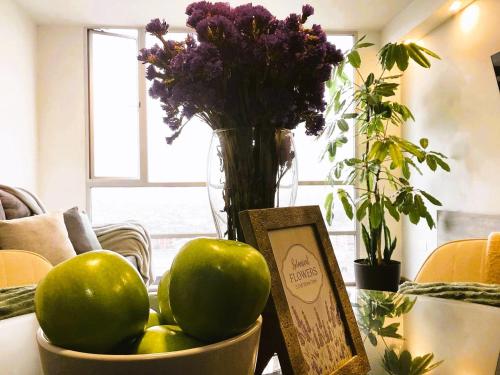 a bowl of apples and a vase with purple flowers at Departamento cerca Solca, Embajada Americana y Estadio Atahualpa con vista al COTOPAXI y la CIUDAD in Quito