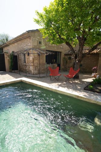 - une piscine avec 2 chaises rouges à côté d'une maison dans l'établissement Le petit Mas du village, à Saint-Rémy-de-Provence