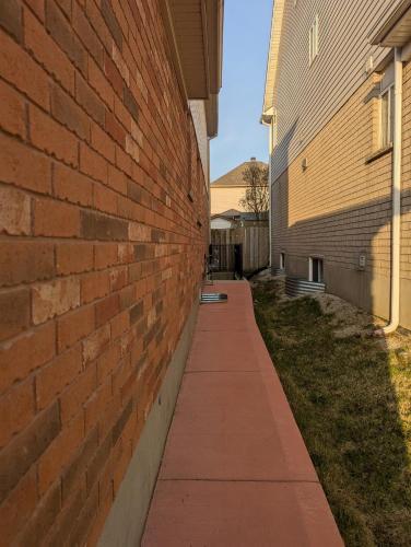 a brick wall with a sidewalk next to a building at Basement two Queen beds and one single with two full washrooms by YKF airport in Kitchener