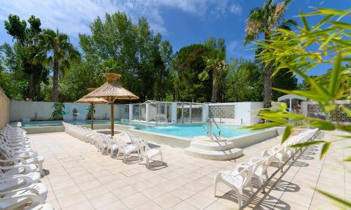 - une piscine avec des chaises blanches et un parasol dans l'établissement L'Eden - Mobil home 2 chambres 6 personnes Piscine, au Grau-du-Roi