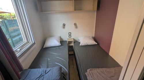 two beds in a room with a window at Mobil home haut de gamme 6 personnes camping 4 étoiles Marvilla Parks BARCARES plage in Torreilles