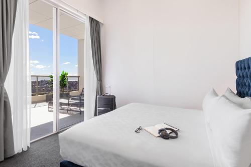 a bedroom with a white bed and a balcony at Meriton Suites Bondi Junction in Sydney
