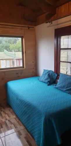 a bedroom with a blue bed with a window at Cabañas Pozo Azul in El Quisco