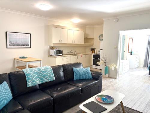 a living room with a black leather couch and a kitchen at Smugglers On The Beach in Coffs Harbour