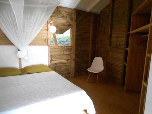 a bedroom with a white bed and a chair at Nati Lodge - Bungalow Guadeloupe in Bouillante