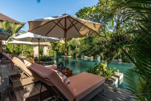 een patio met stoelen en een parasol naast een zwembad bij Radha Phala Resort & Spa in Ubud