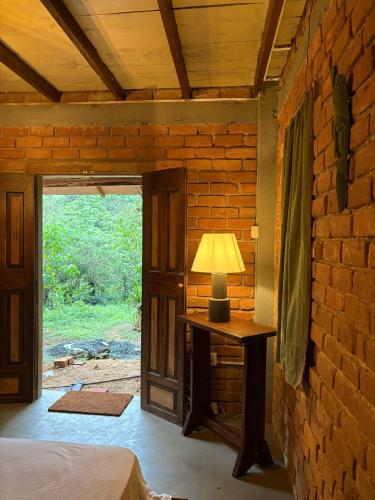 a bedroom with a lamp on a table next to a brick wall at Wild hikes River Escapes & Nature Views with Meals in Badureliya