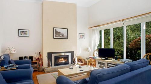 sala de estar con sofás azules y chimenea en Crabapple Southside Mountain Cottage Pet Friendly, en Wentworth Falls