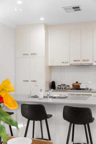 a white kitchen with two chairs and a sink at Clay and Clover in Thebarton