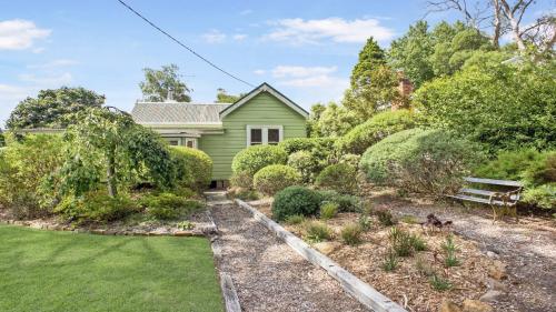 a green house with a bench in the yard at Quinees Charming Mountain Cottage in Blackheath