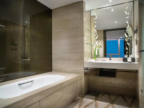 a bathroom with a tub and a sink and a mirror at Sofitel Lianyungang Suning in Lianyungang