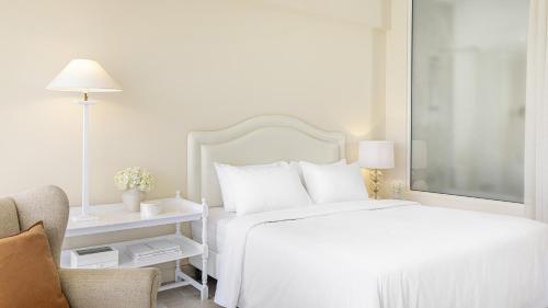 a white bedroom with a bed and a chair at Grecotel Eva Palace in Kommeno