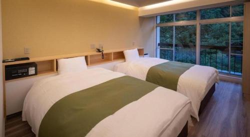 two beds in a hotel room with a window at Hotel Myoken Tanaka Kaikan in Kirishima