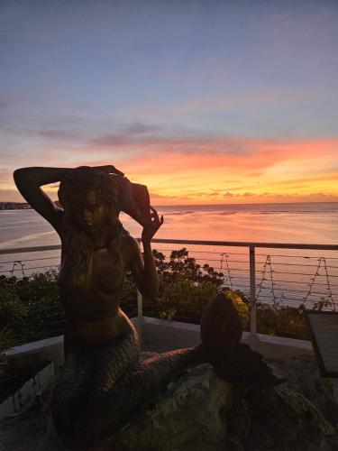 a statue of a mermaid sitting on a wall with a sunset at Guam Reef Hotel in Tumon