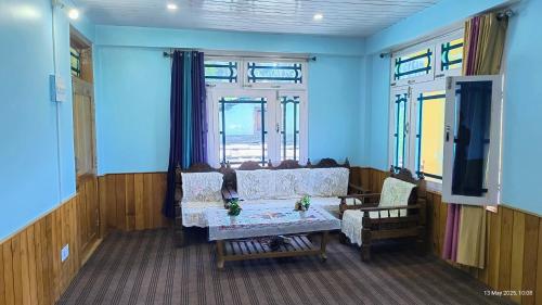 a living room with a couch and a table and windows at Aurelia by Xtastays - Deohari, Sainj Valley, Kullu in Sainj