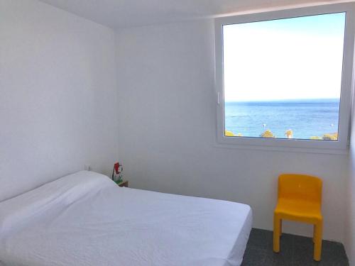 a bedroom with a bed and a yellow chair and a window at Cosy apartment with fabulous SEA VIEWS 70's style in Sant Feliu de Guixols