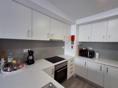 a white kitchen with white cabinets and a black appliance at Smile and Wave Apartment in Ponta Delgada