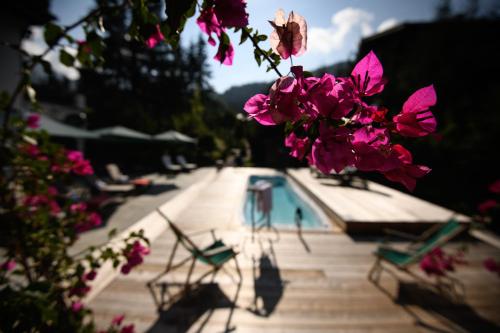 a pool with two chairs and pink flowers in the foreground at House of Hütter - Wachtelhof & SPA in Maria Alm am Steinernen Meer