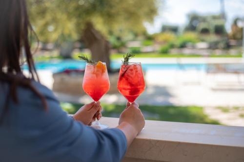 a woman holding up two cocktails on a railing at Masseria Galleppa by Apulia Hospitality in Monopoli