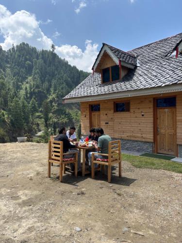 a group of people sitting at a table in front of a cabin at Apple Land by Naavagat in Jibhi