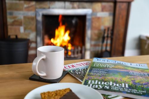 een tafel met een bord taart, een kopje en een boek bij Brambly Cottage in Whitby