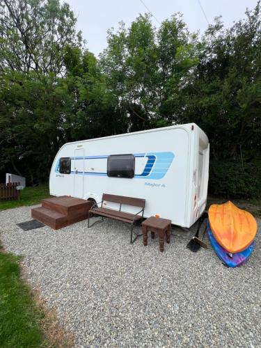 a white rv parked on the gravel with a bench and tables at Seaview Retreat & Sauna at An Acre By The Sea in Clonakilty