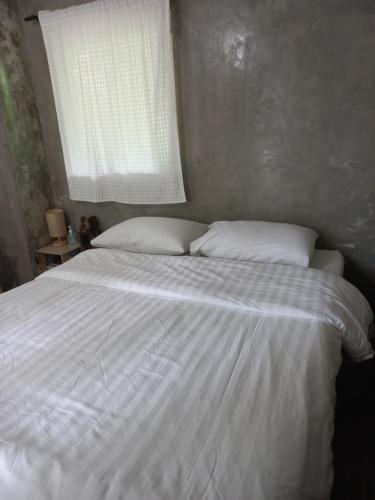 a white bed with two pillows and a window at บ้านพักคุณยายเขียว in Ban Thung Kham