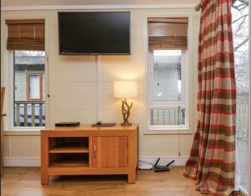a living room with a tv on a wall with windows at Brook Lodge in Troutbeck Bridge
