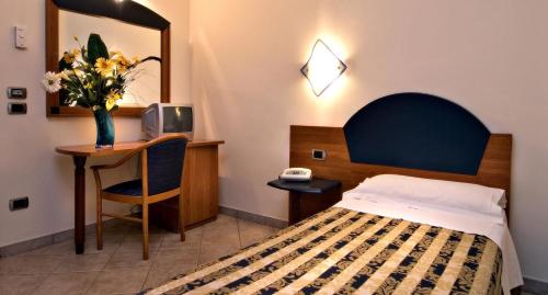una camera con letto e scrivania con vaso di fiori di Hotel Marconi a Pietraperzia
