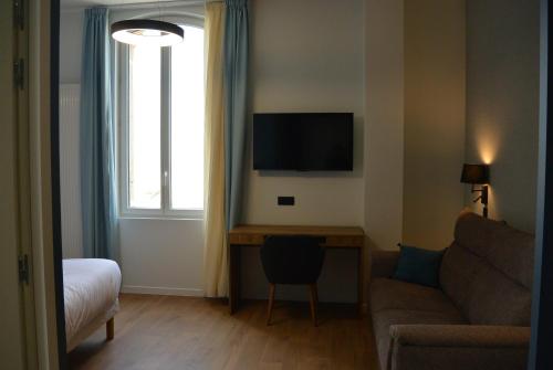 a living room with a couch and a desk with a television at Les Tourelles Village de vacances in Asnelles