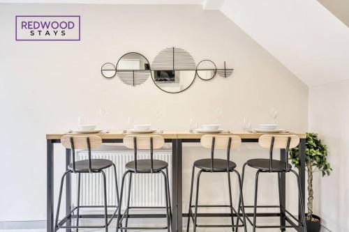 a kitchen with a bar with four stools at Huge 5 Bed 3 Bath House For Contractors & Families, 2X Free Parking, Free WiFi & Netflix By Redwood Stays in Farnborough