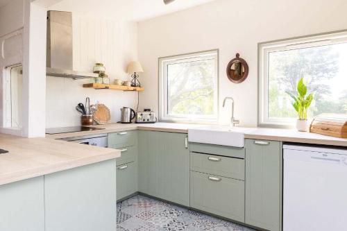 a kitchen with white and green cabinets and windows at Historic Railway Home - Selsey Seafront in Selsey