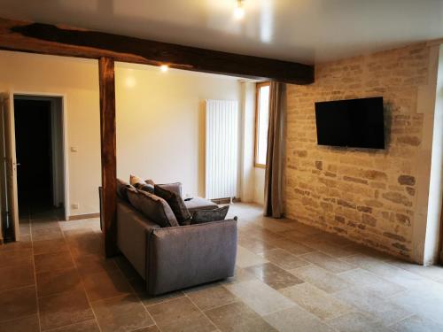 a living room with a couch and a tv on a brick wall at La Maison d'Hortense au coeur du vignoble in Saint-Bris-le-Vineux