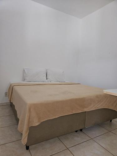 a bed with a tan blanket and a white wall at Cantinho da LAGO in Itacuruçá