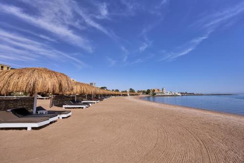 a beach with a bunch of chairs and a straw umbrella at Turtle's Inn Hotel in Hurghada